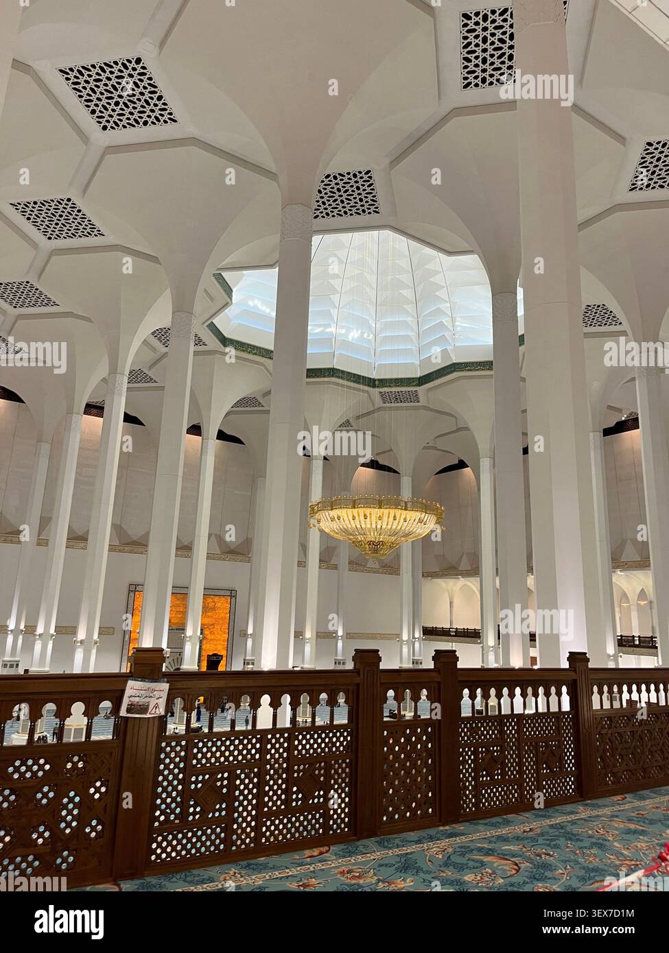 Prächtiges Interieur der Großen Moschee mit eleganten weißen Säulen, islamischer Architektur, großem goldenen Kronleuchter und geometrischen Deckenmustern - Smartphone-aufgenommenes Stockfoto