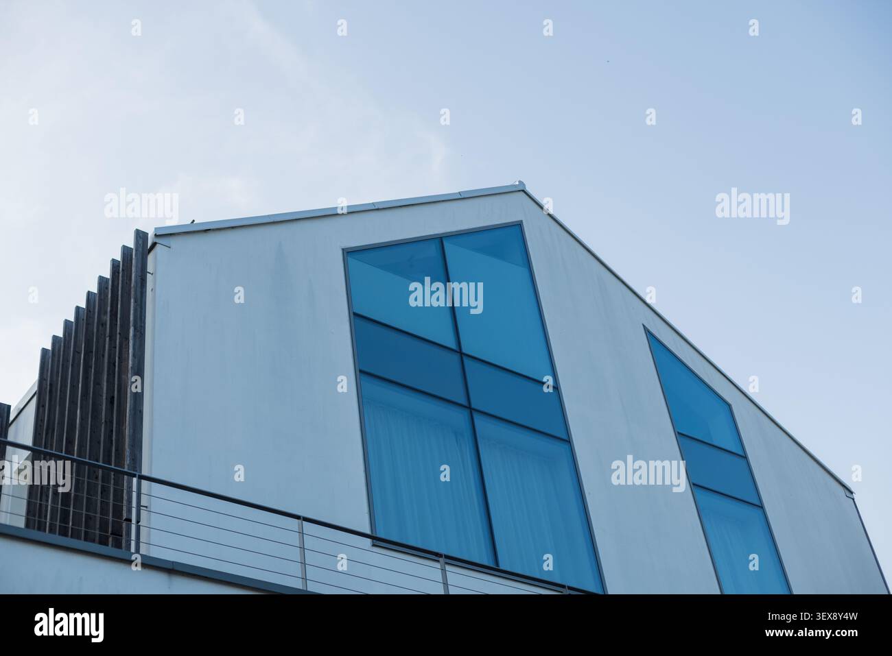 Moderne, minimalistische Hausfassade mit blau getönten Fenstern vor klarem Himmel. Zeitgenössische nordische oder skandinavische Wohnarchitektur. Stockfoto