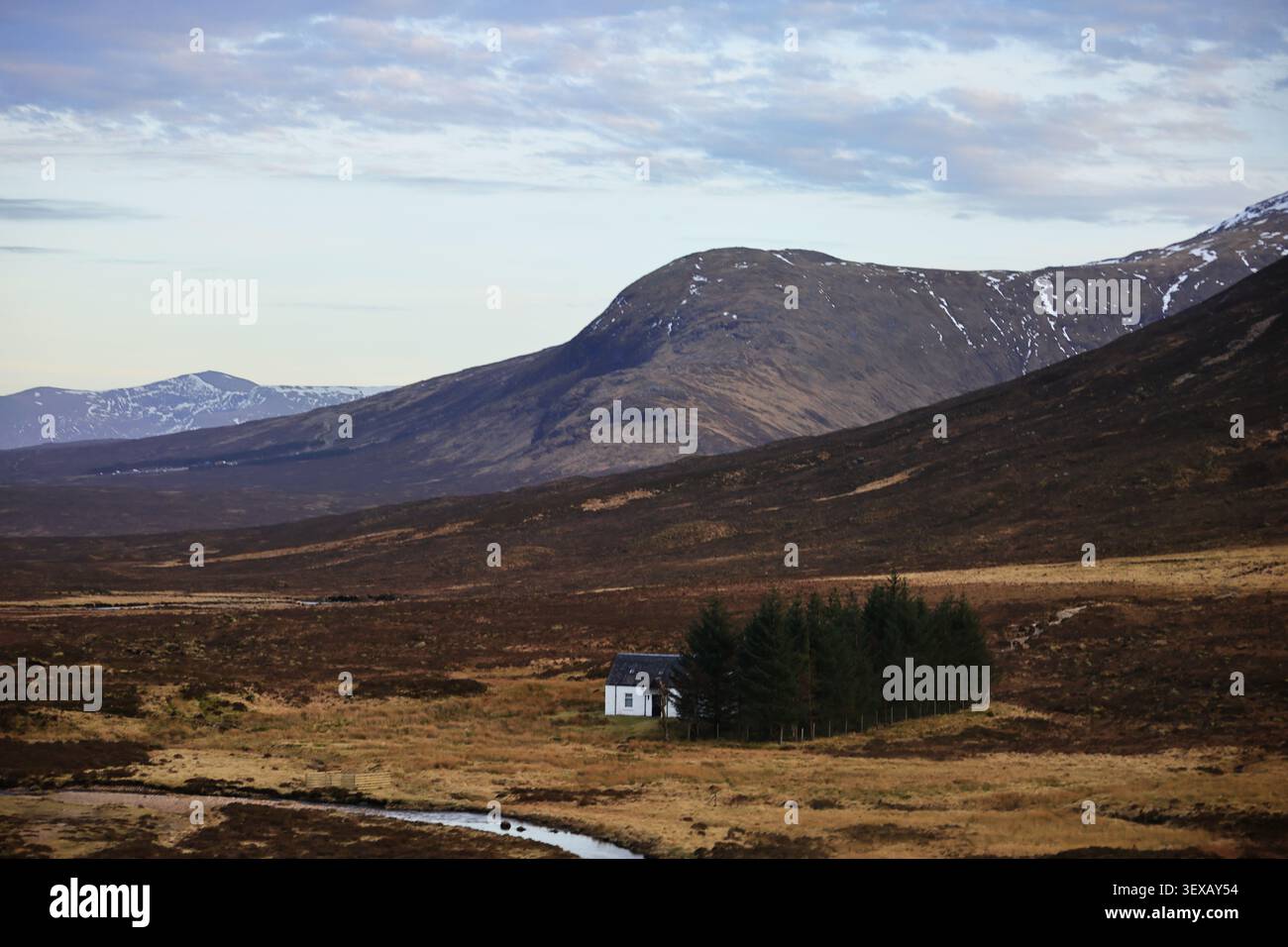 Three Sisters of Glencoe Area in den schottischen Highlands verfügt über ein weites Bergtal, ein kleines weißes Gebäude und ein dunkles Moor mit hellem Himmel. Stockfoto