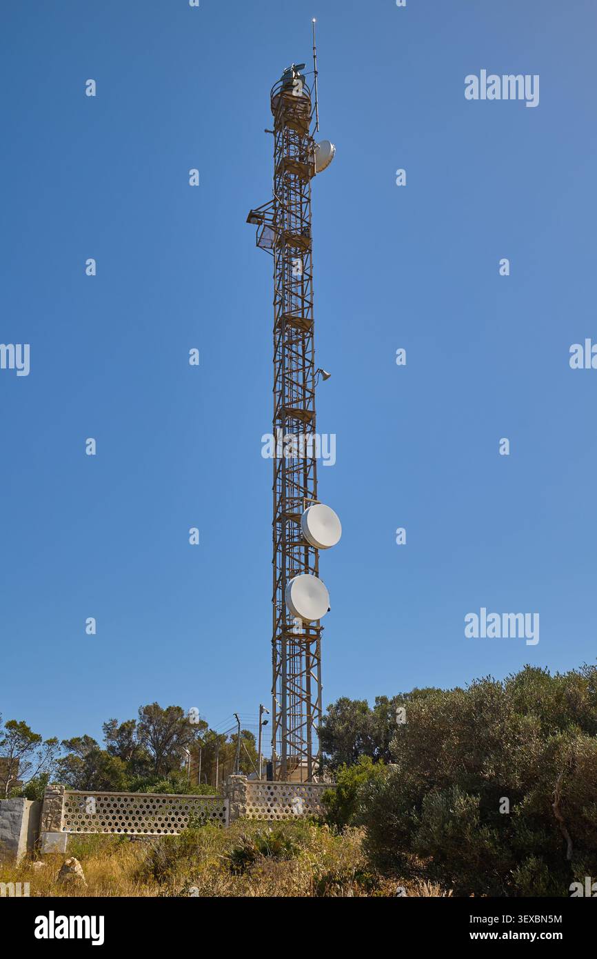 Telekommunikationsturm aus Metall, ausgestattet mit verschiedenen Kommunikationsantennen und Sendern unter klarem blauen Himmel, repräsentiert moderne drahtlose Technologie Stockfoto