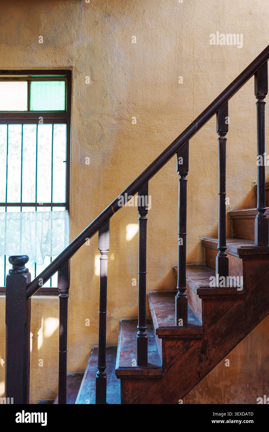 Alte Holztreppe mit rustikalem Handlauf und strukturierter, gelber Wand und Vintage-Fenster im chinesischen Haus Stockfoto