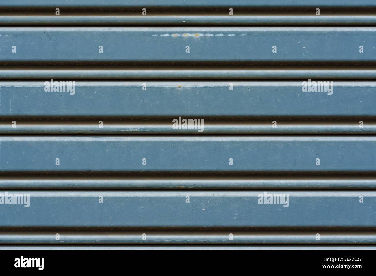 Blau und grau lackierte Metall Rollladen Garagentor Oberfläche mit gewellten Reihen subtile Rostflecken und abgenutzte Farbe industrielle Textur Hintergrund Stockfoto