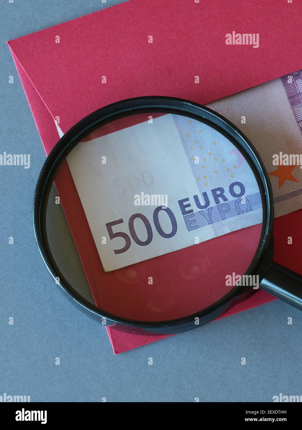 Versteckte 500-Euro-Banknote in rotem Umschlag unter Vergrößerungsglas als Symbol für geheimes Bargeld und Finanzbetrug Stockfoto