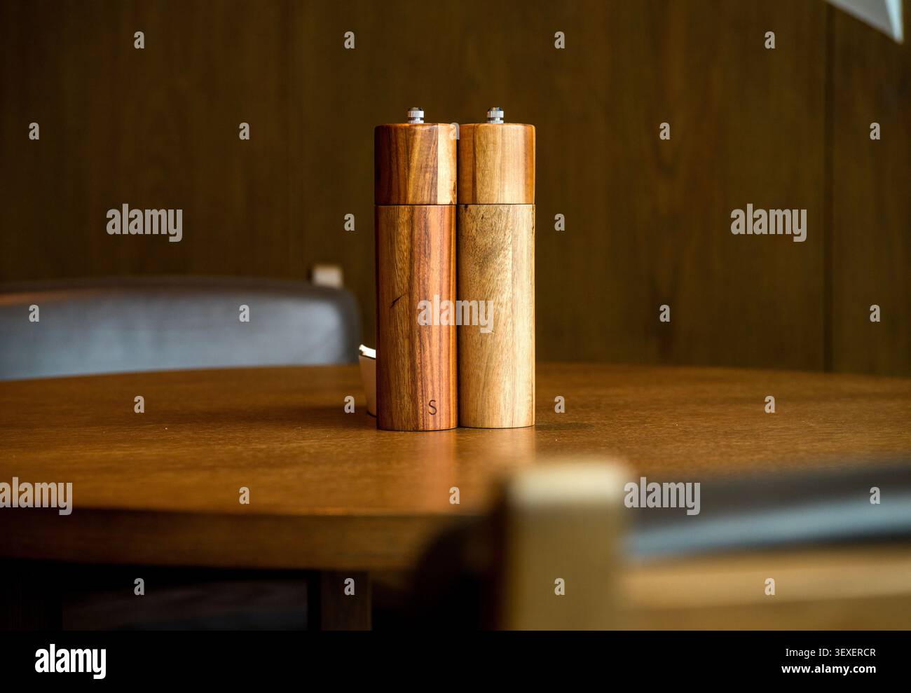 Ein Paar eleganter Salz- und Pfeffermühle aus Holz, die auf einem polierten Tisch in einem warmen, gemütlichen Restaurant stehen. Stockfoto