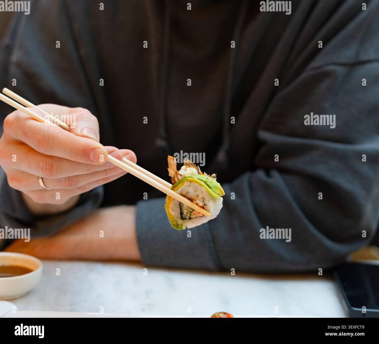 Eine Nahaufnahme einer kalifornischen Rolle, die von Stäbchen gehalten wird, mit wunderschöner Präsentation und kunstvoller Beschichtung. Das appetitliche Arrangement betont frische Zutaten und das sorgfältige Styling japanischer Speisen Stockfoto