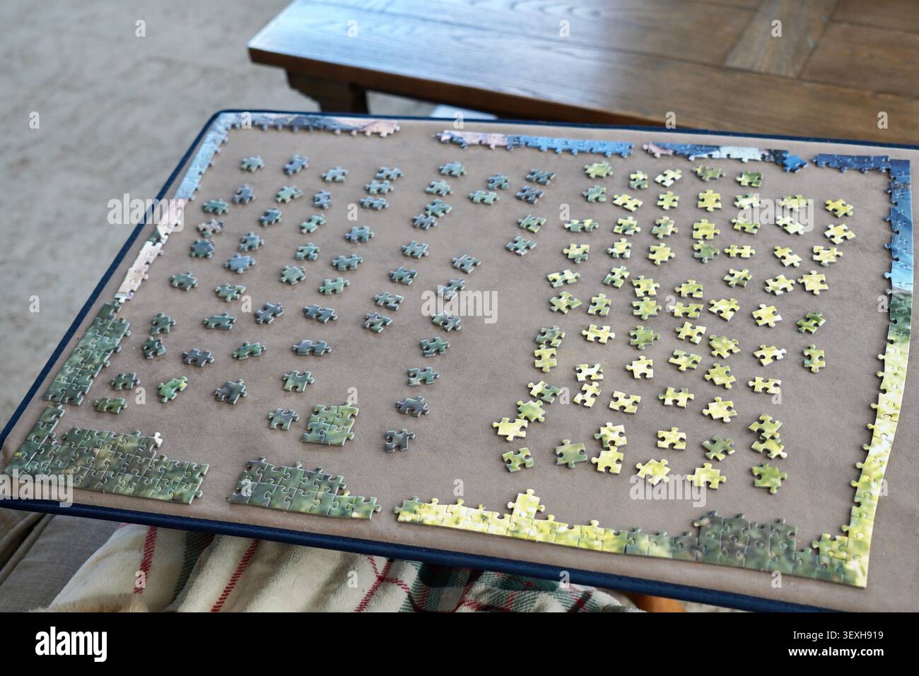 Puzzleteile auf einem Puzzlebrett mit Grüntönen, Gelbtönen und Blautönen Stockfoto