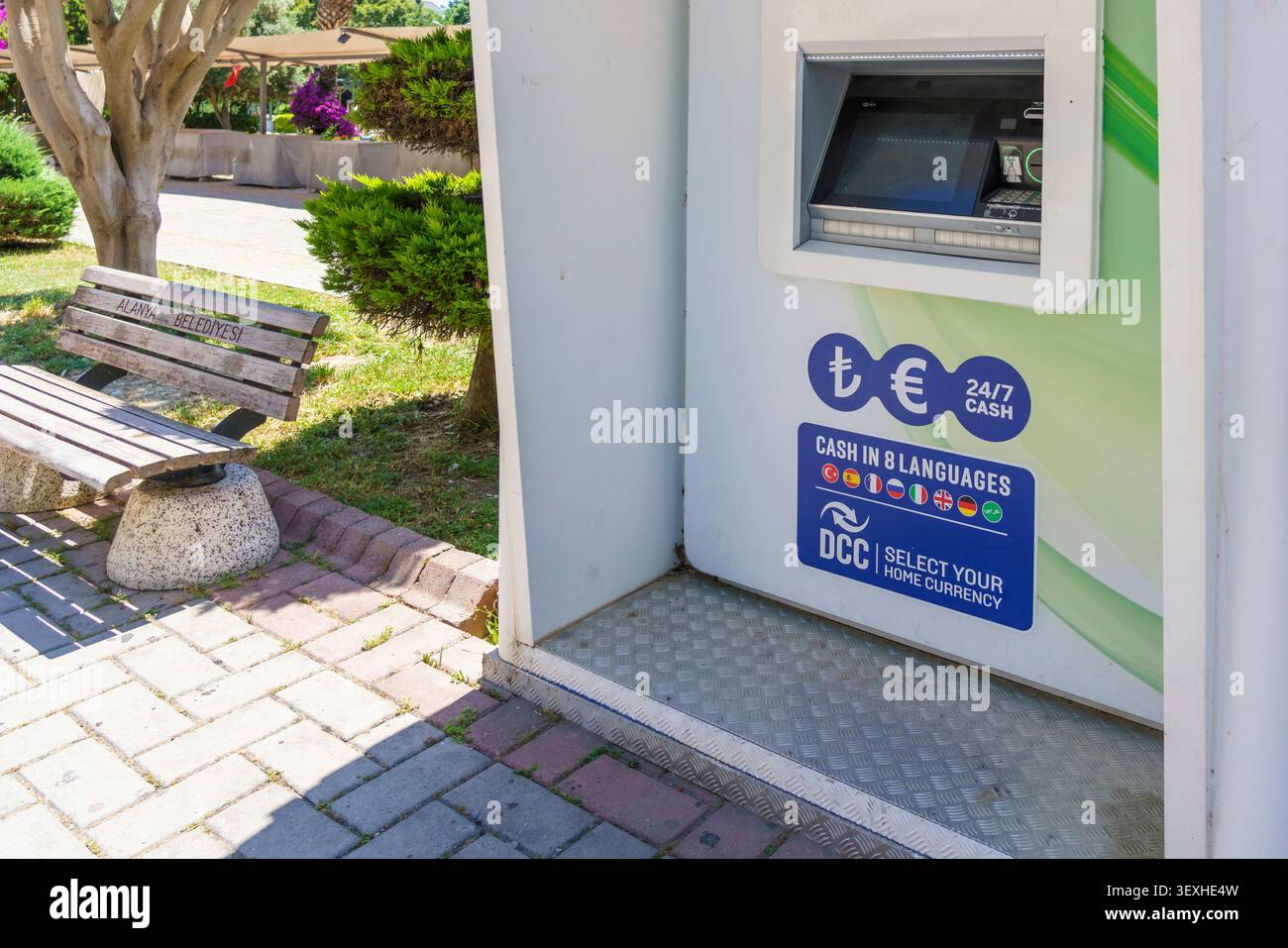 Der Geldautomat bietet Geldauszahlungen in mehreren Währungen in einem Park mit Bank und Gartenanlagen in der Nähe Stockfoto