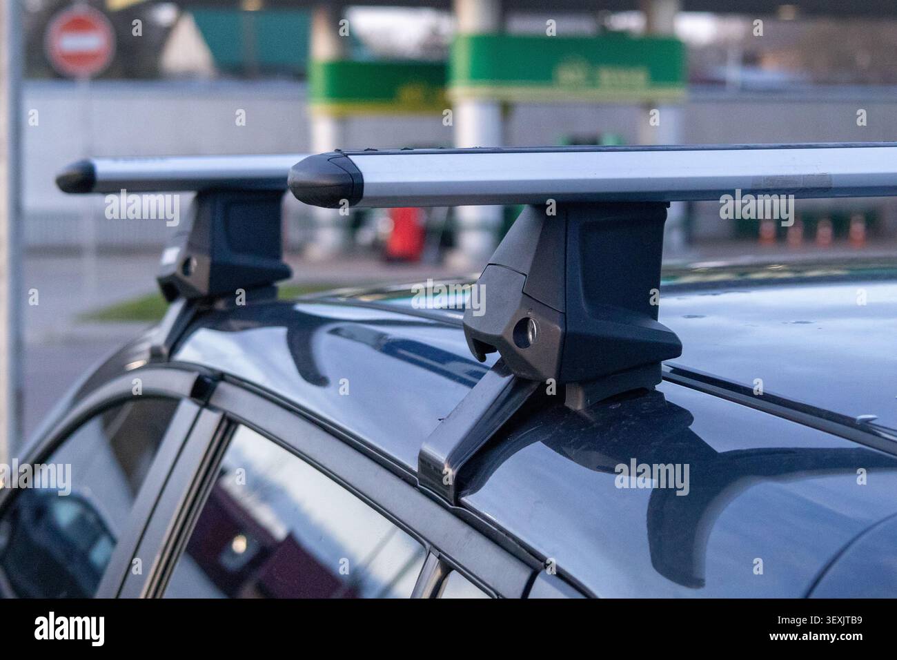 Autodachträger sind sicher an einem Fahrzeug befestigt, das auf einem Parkplatz in der Nähe einer Tankstelle geparkt ist. Die Szene zeigt einen klaren Himmel und andere Autos dahinter. Stockfoto