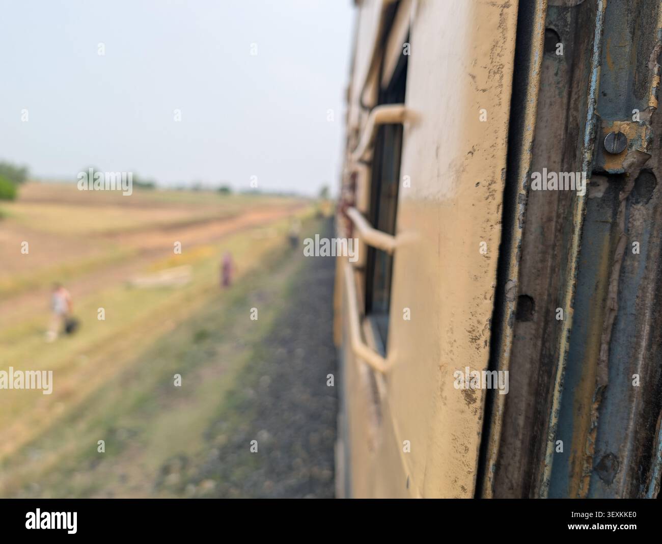 Nahaufnahme aus der Nähe eines fahrenden indischen Personenzugs mit Außenwagen mit verschwommener ländlicher Landschaft und landwirtschaftlichen Feldern in Nordindien. - Smartphone-aufgenommenes Stockfoto