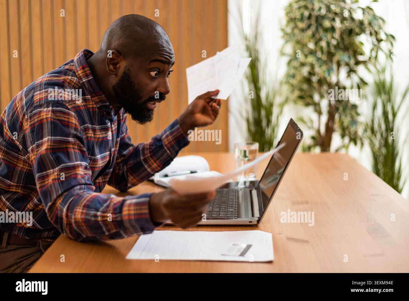 Von Papierkram überwältigt, kämpft ein Mann, um seine Finanzen zu organisieren, während er von zu Hause aus arbeitet. Stockfoto