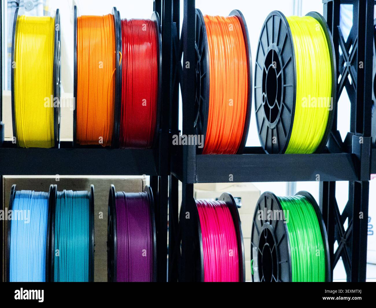 Eine Vielzahl von leuchtenden Filamentspulen für den 3D-Druck in mehreren Farben sind auf schwarzen Regalen ordentlich angeordnet und für die additive Fertigung und Prototypen bereit Stockfoto