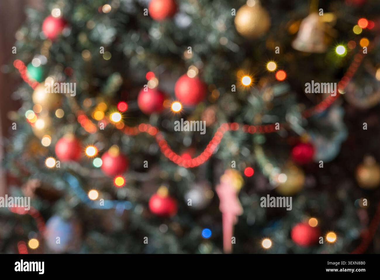 Horizontale Nahansicht eines verzierten Weihnachtsbaumzweigs mit Ornamenten wie Sternen, Glocken und roten und goldenen Kugeln. Warm glühende Fee l Stockfoto