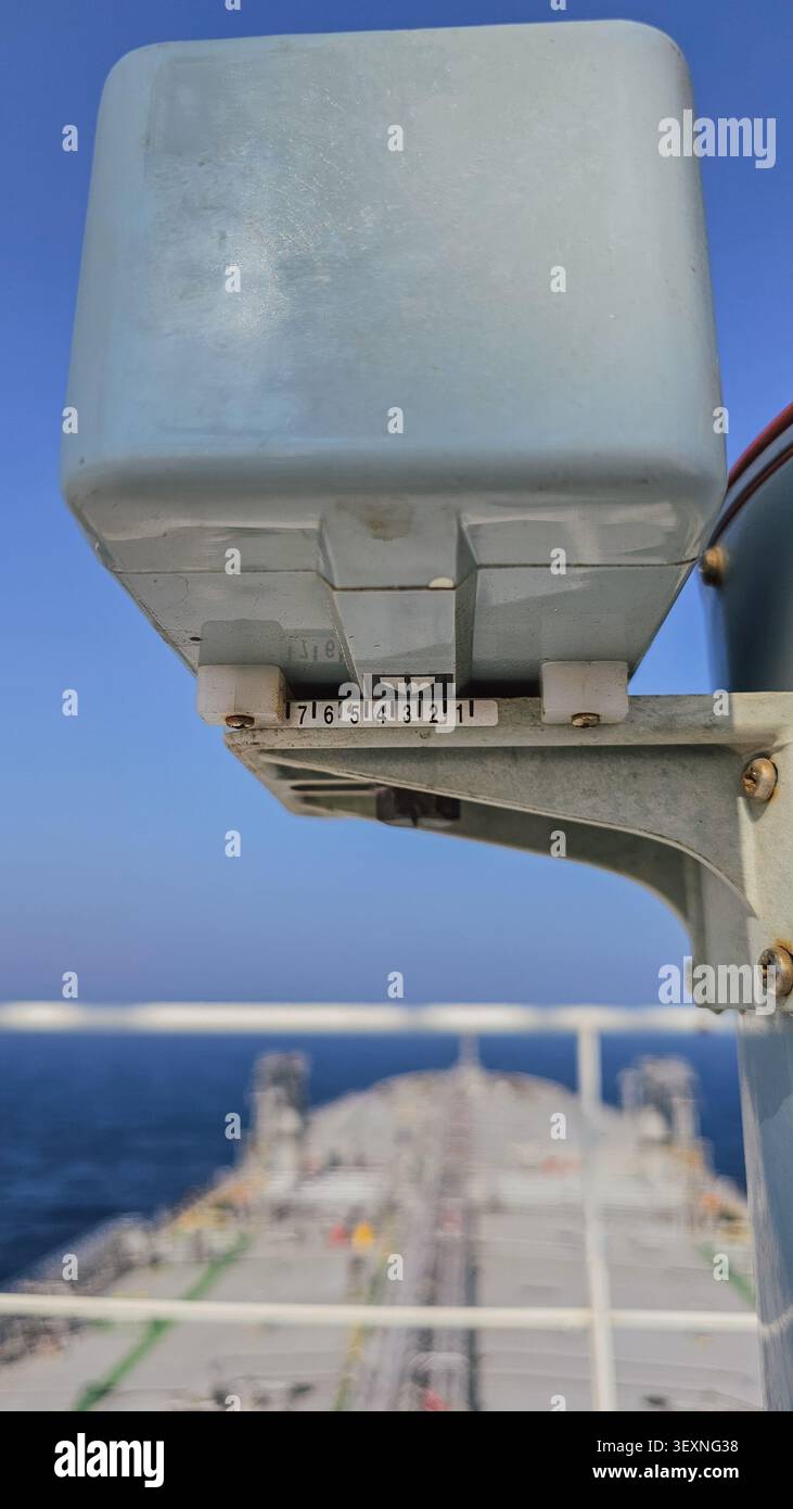 Vertikale Nahaufnahme eines Meeresstandsanzeigers mit einer nummerierten Skala auf einem Schiffsdeck, mit dem verschwommenen Bug des Tankers und dem blauen Ozean in BA Stockfoto