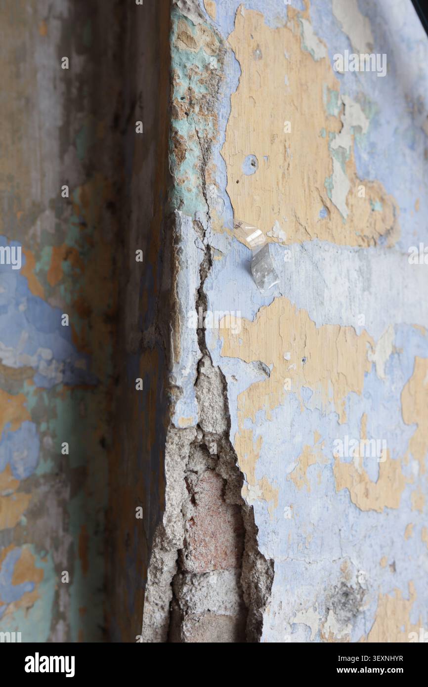 zeigt abgeplatzten Putz, der das darunter liegende Ziegelmauerwerk freilegt, unter abblätternder blauer, beiger und weißer Farbe in einer Wand Ecke. Stockfoto