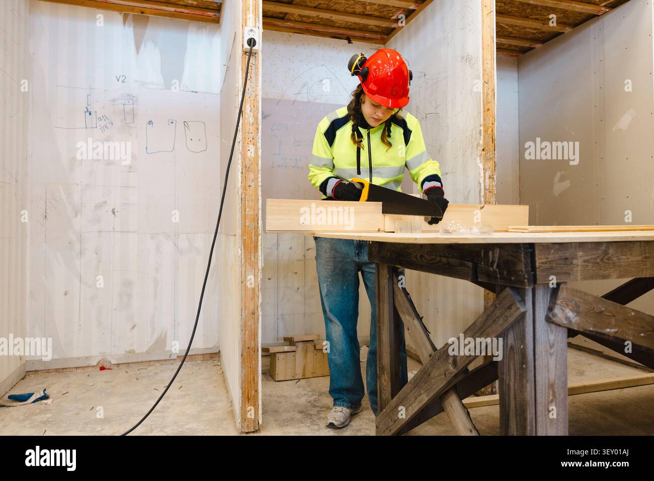 Die gesamte Länge einer jungen Berufsschülerin, die Holzplanke mit Handsäge beim Training in der Sekundarschule sägt Stockfoto