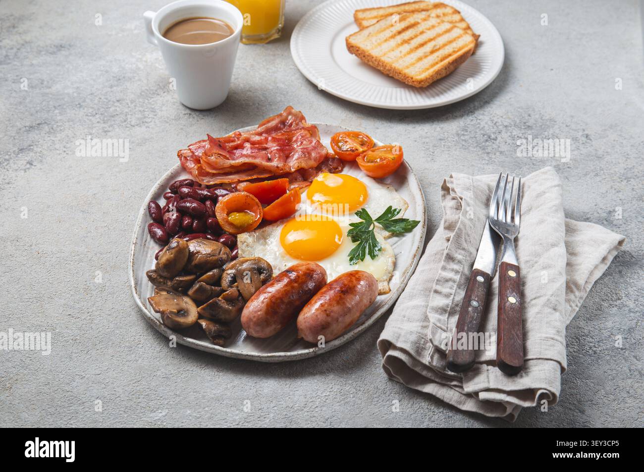 Komplettes englisches Frühstück auf einem warmen, einladenden Tisch mit Keramikplatten und Besteck mit Holzgriff, Blick von oben auf das morgendliche Essen Stockfoto
