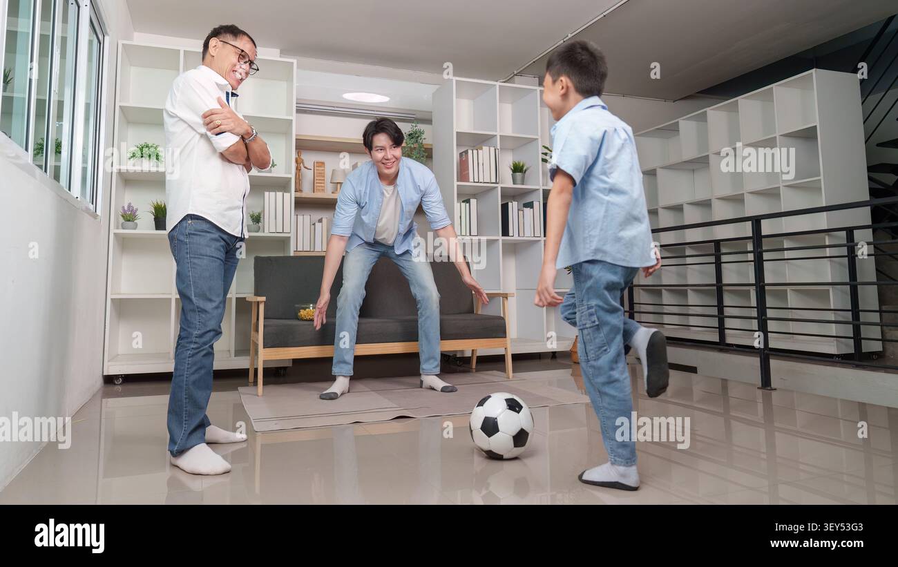 Eine generationenübergreifende asiatische Familie, die gemeinsam Fußball im Wohnzimmer spielt Stockfoto