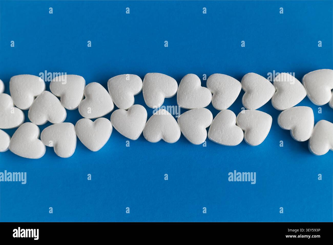 Horizontale Linie herzförmiger Pillen auf blauem Hintergrund. Symmetrisches Layout mit doppeltem Abstand für Text (oben und unten) für Medizin und Pharmazie Stockfoto