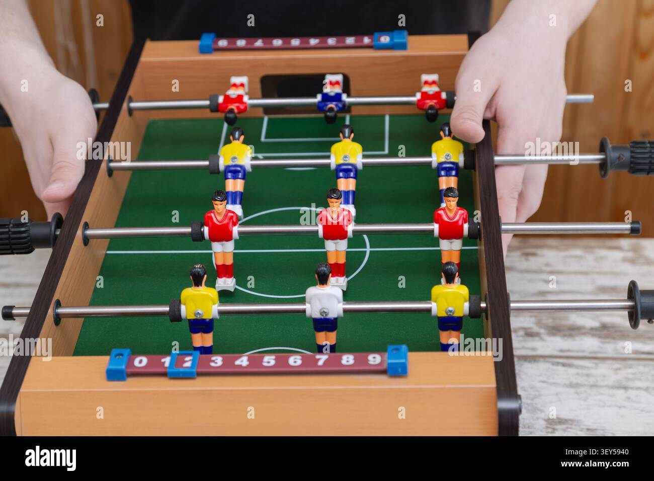 Nahaufnahme von Händen, die ein Mini-Tischkicker mit bunten Spielfiguren auf einem grünen Feld greifen. Familienunterhaltung, Indoor lei Stockfoto