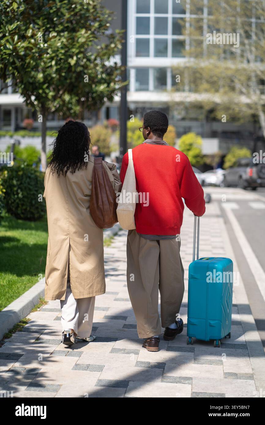 Modisches verheiratetes Paar afroamerikanische Reisende, die mit Koffern auf der Straße spazieren gehen. Stockfoto