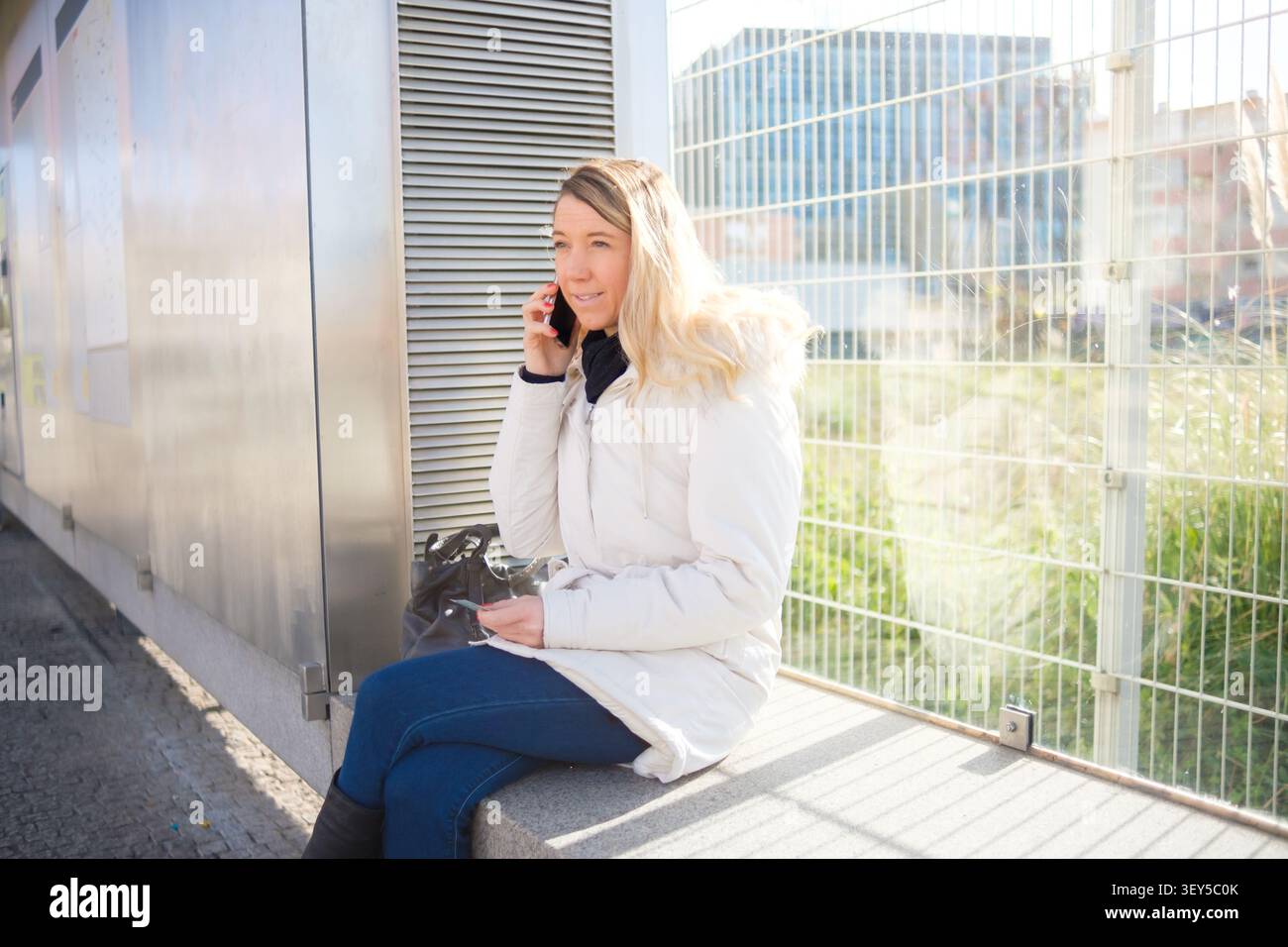 Frau, die am Telefon kommuniziert, während sie auf einer Bank im Stadtgebiet sitzt Stockfoto
