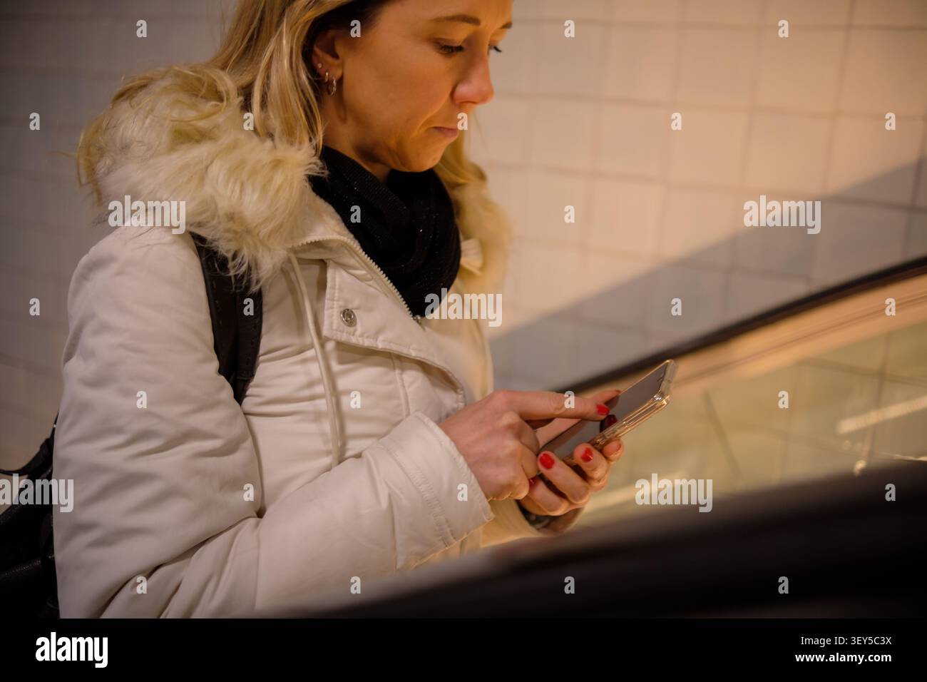 Frau, die ein Smartphone auf einer Rolltreppe benutzt und sich in einer städtischen Umgebung mit Technologie verbindet Stockfoto