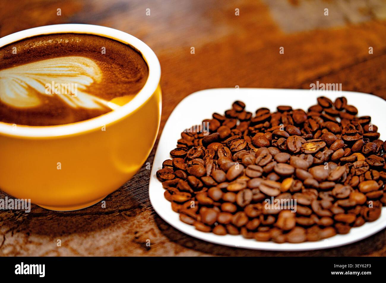 Eine Tasse Kaffee, dekoriert mit einem Herz und Kaffeebohnen auf einem weißen Teller. Dunkler Hintergrund Stockfoto