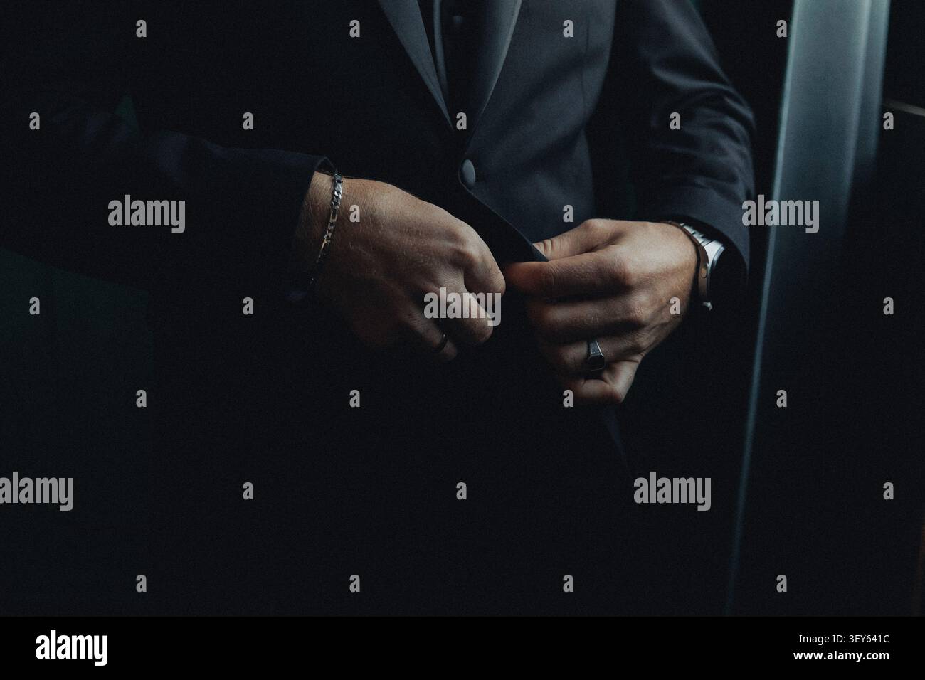In dunkler Kleidung passt der Mann seinen Anzug an. Seine Hände zeigen viel Liebe zum Detail und Präzision. Die Beleuchtung hebt sein Zubehör hervor Stockfoto
