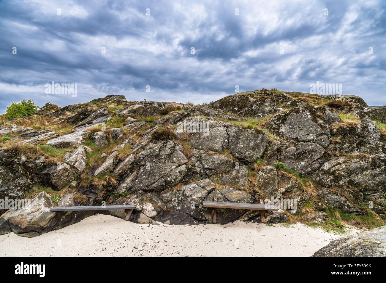 Dramatischer Blick auf eine zerklüftete Küstenklippe mit erodierten Felsschichten und karger Vegetation unter bewölktem Himmel. Stockfoto