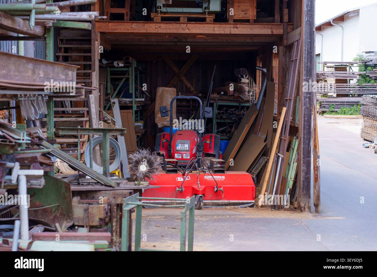 Otzberg-Lengfeld, Deutschland - 15. Juni 2026: Kompakter roter Traktor mit landwirtschaftlichem Anbaugerät in einer überdachten Holzscheune in Werkstatt und Lagerung Stockfoto
