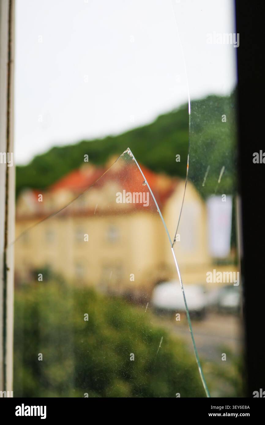 Glassplitter in einem Fensterrahmen mit sichtbarem Riss und zersplittertem Fragment, die Schäden an Häusern, Unfällen, Einbrüchen oder Sicherheitsrisiken symbolisieren. Stockfoto
