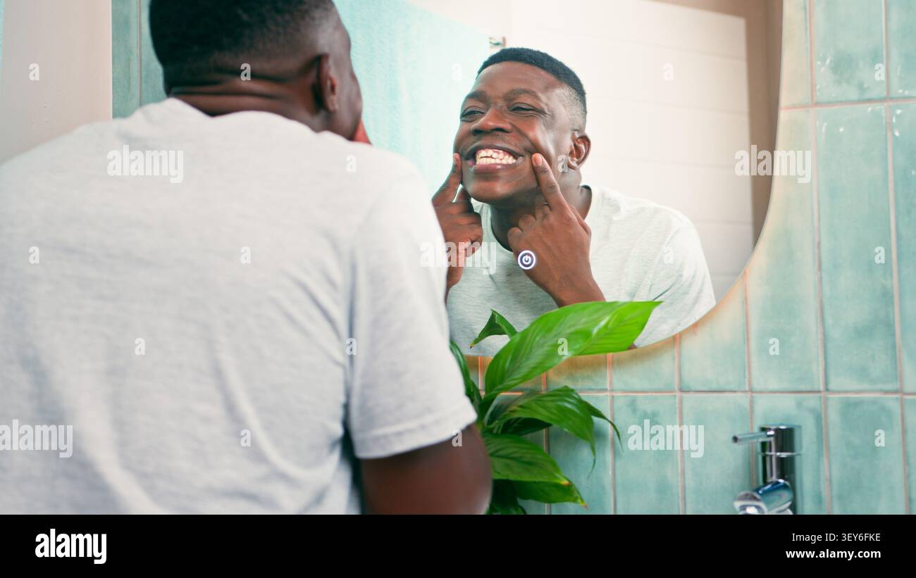 Mann lächelt im Spiegel, während er die Zähne während der morgendlichen Badezimmerhygiene überprüft Stockfoto