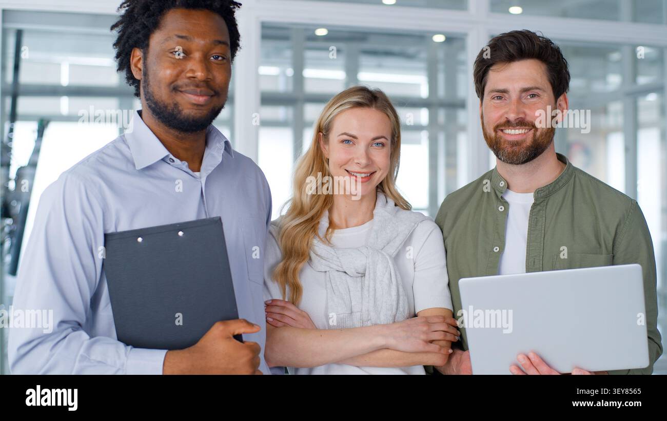 Multiethnische Unternehmensgruppe drei Kollegen, die in die Kamera schauen, lächeln glücklich im Firmenbüro Projektteam afrikanische und kaukasische Geschäftsleute Stockfoto