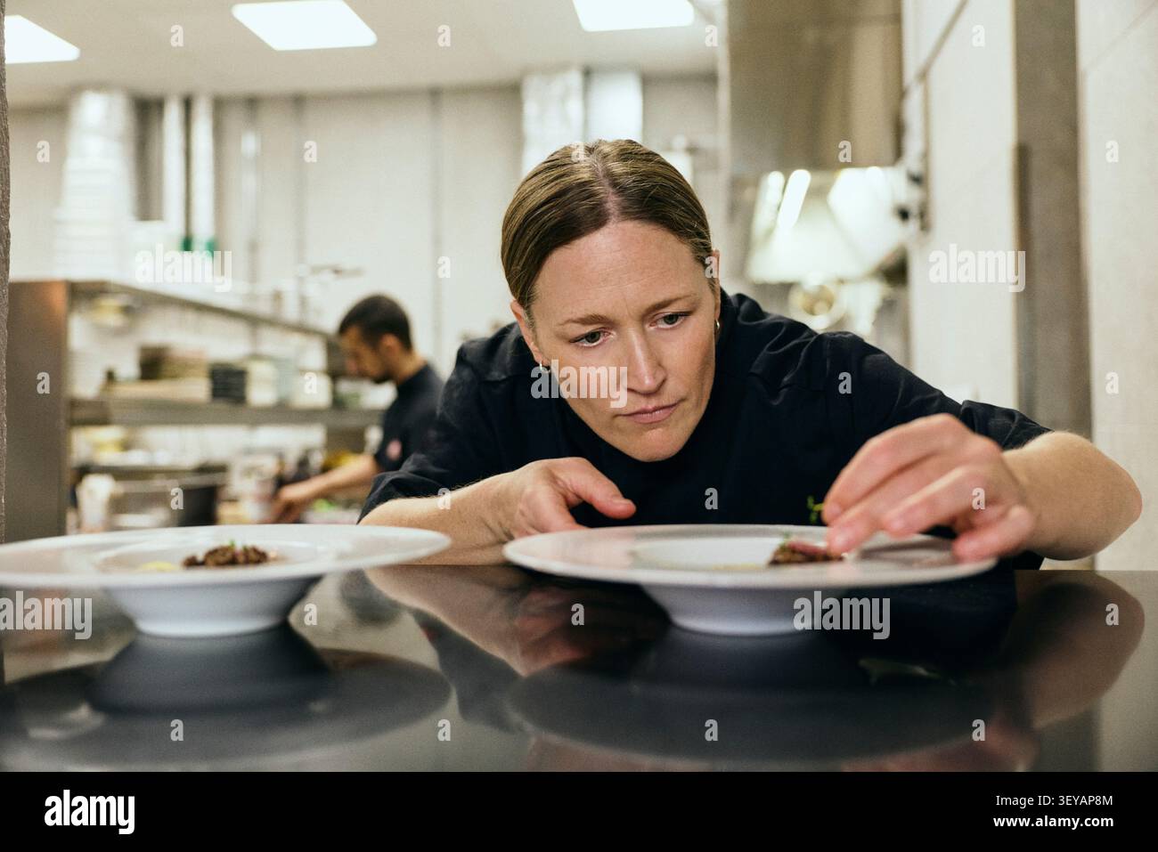 Die konzentrierte Chefkochin fügt dem Gericht vor dem Servieren letzte Details hinzu Stockfoto