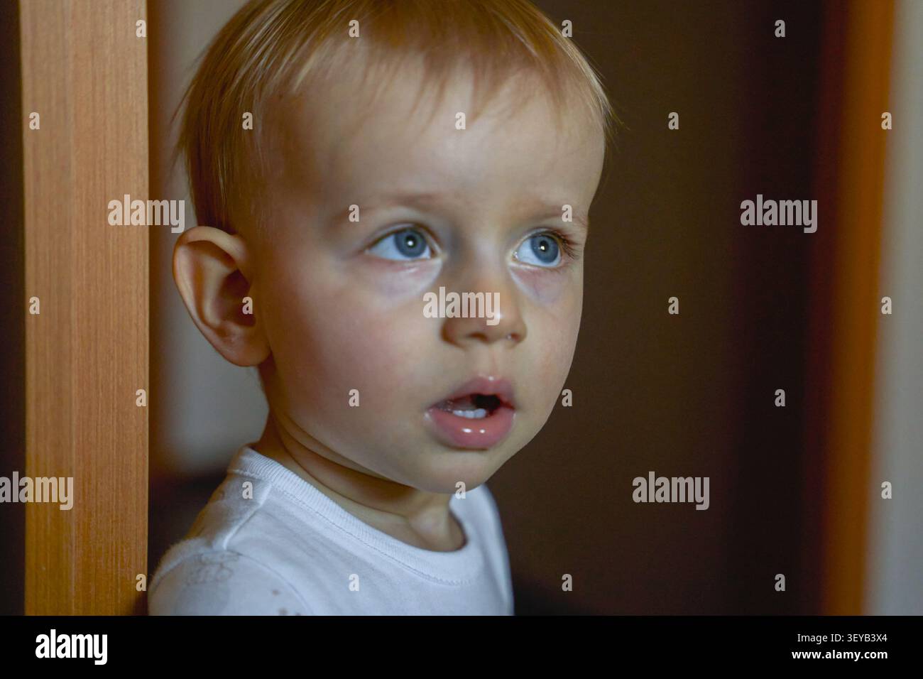 Nachdenklicher Junge, 2 Jahre alt, mit offenem Mund, der nach oben blickt, Junge mit europäischem Aussehen mit blauen Augen, ist zu Hause. Hochwertige Fotos Stockfoto