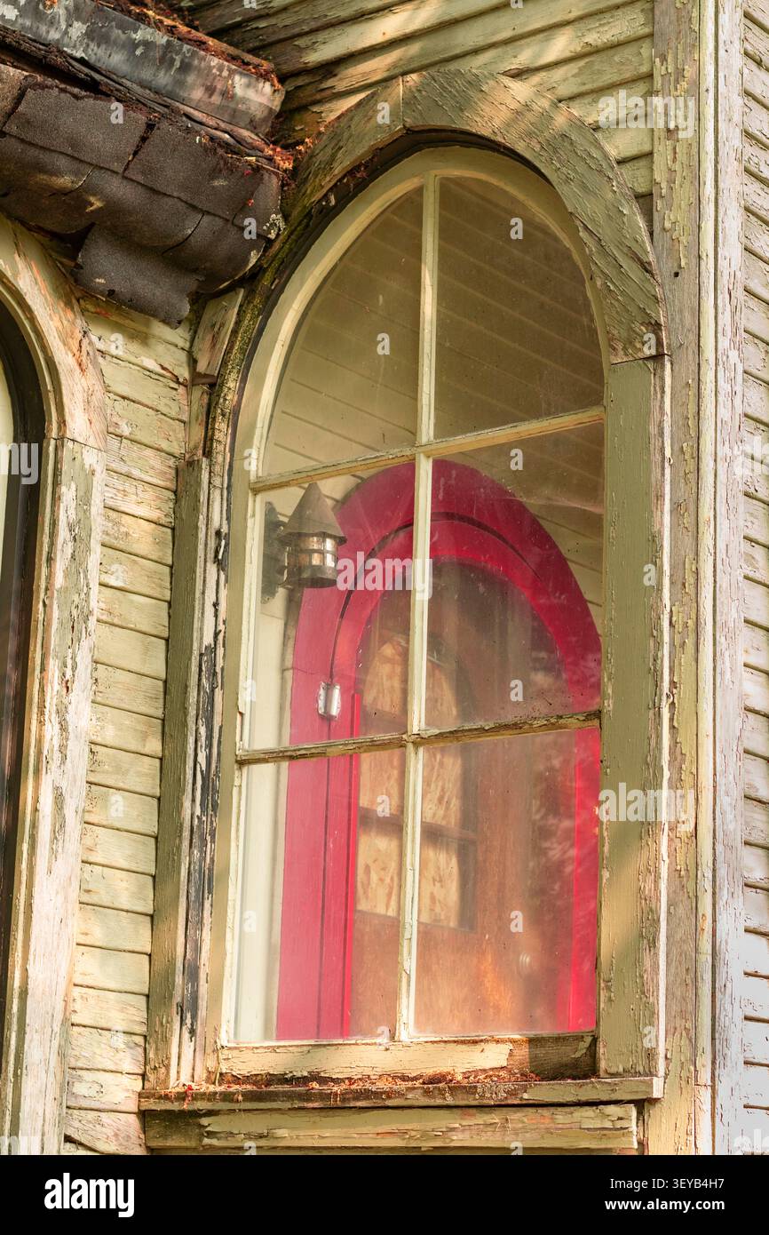 Ein Blick auf eine Bildschirmtür durch ein bogenförmiges Fenster auf einem verlassenen Haus. Stockfoto