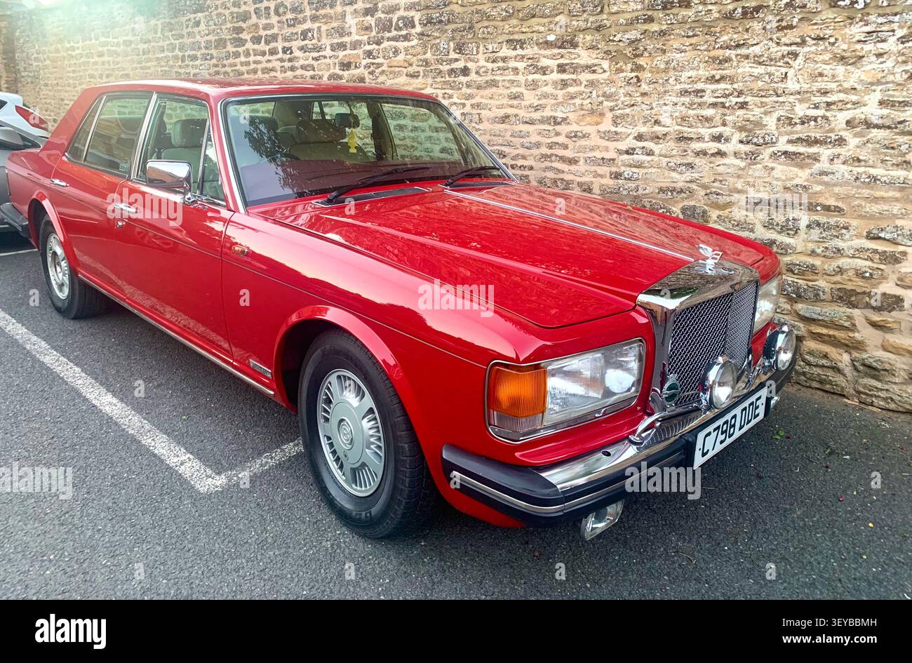 Klassischer roter Rolls Royce Silver Spur, der neben einer Steinmauer auf dem Parkplatz eines Dorfpubs geparkt ist und das britische Luxusdesign und die Handwerkskunst der 1980er Jahre präsentiert - Smartphone-aufgenommenes Stockfoto