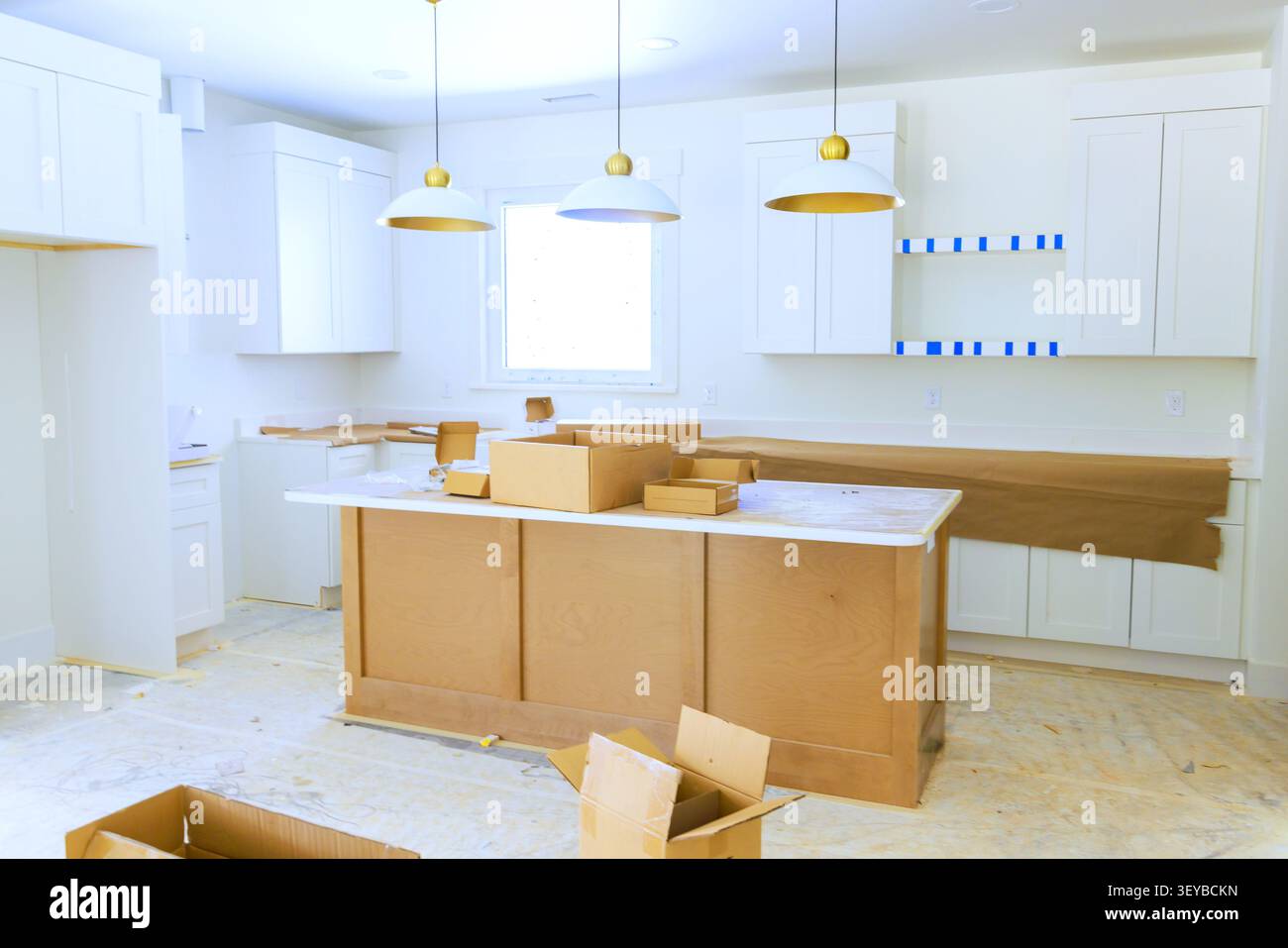 Die Arbeiter richten neue Schränke ein, die Arbeitsflächen im Küchenbereich sind mit Kisten und Verpackungsmaterialien gefüllt. Stockfoto
