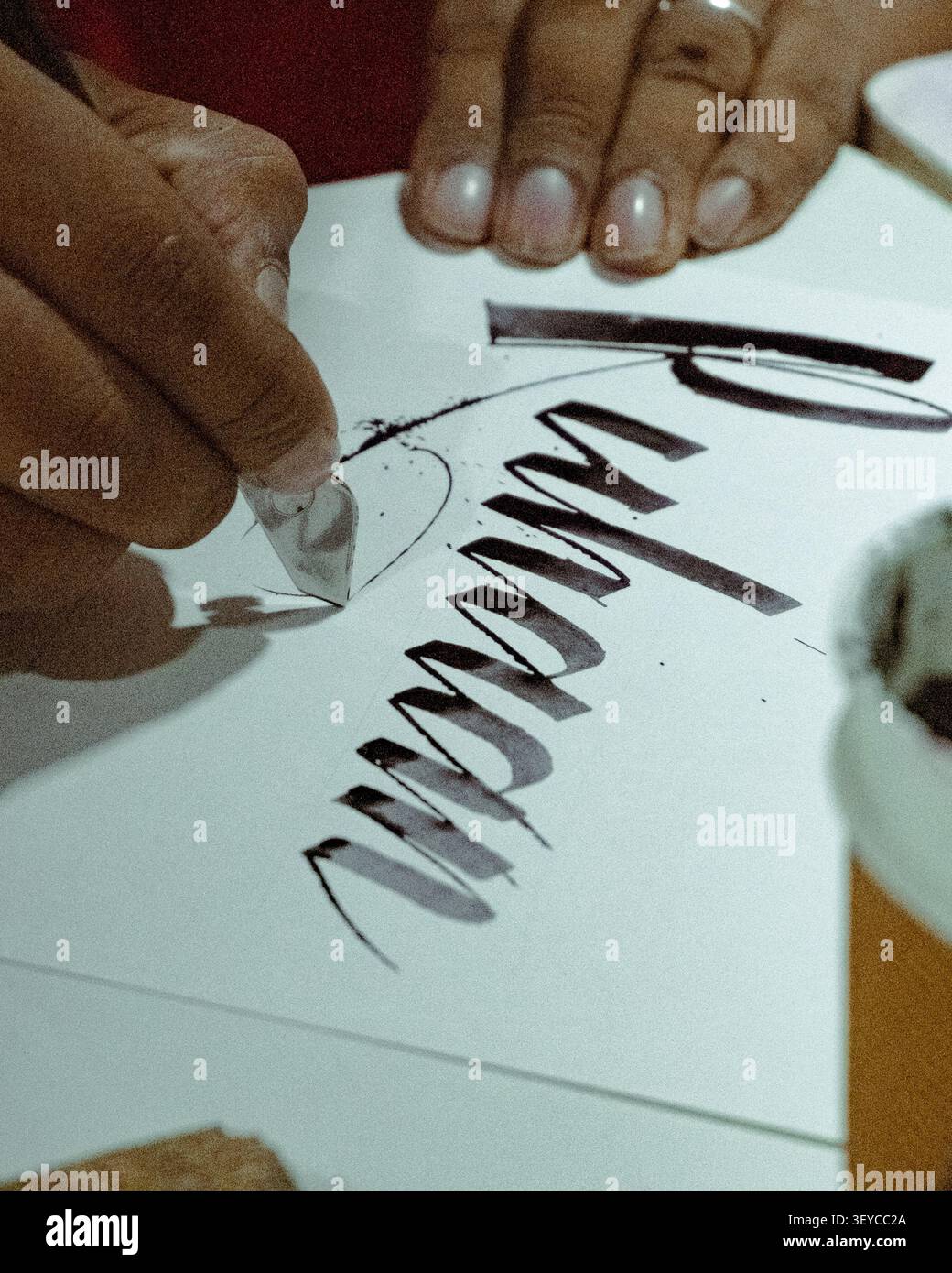 Nahaufnahme eines Kalligraphen, der während einer Kalligrafie-Übungssitzung moderne Handbeschriftungen mit einem Tauchstift und schwarzer Tinte auf weißem Papier erstellt. Stockfoto
