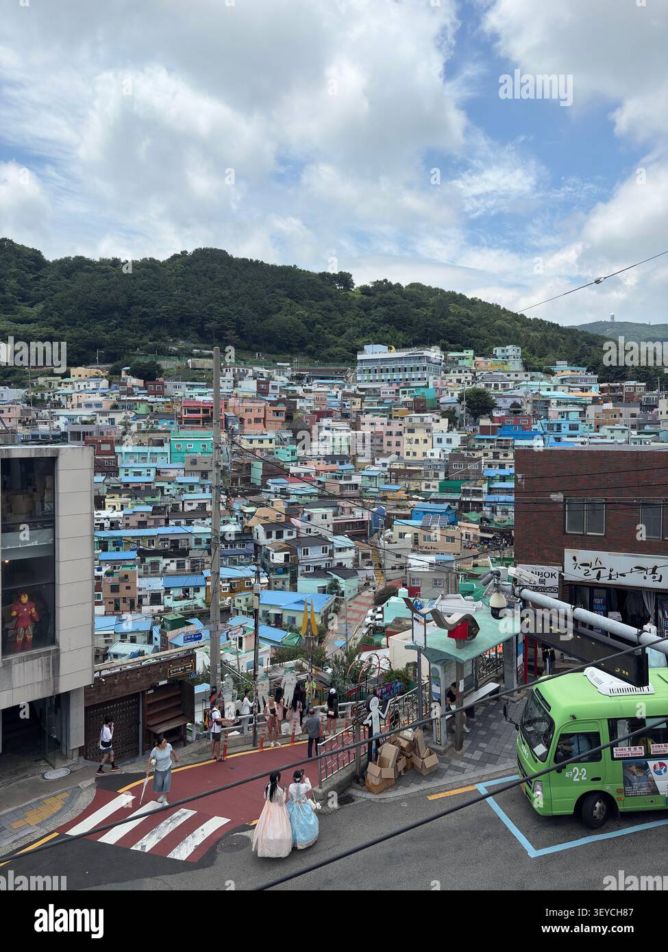 Panoramablick auf Gamcheon Culture Village, Busan, Südkorea. Dicht gepackte pastellfarbene Häuser kaskadieren den Hügel hinunter, von einem geschäftigen Stree aus gesehen - Smartphone-aufgenommenes Stockfoto
