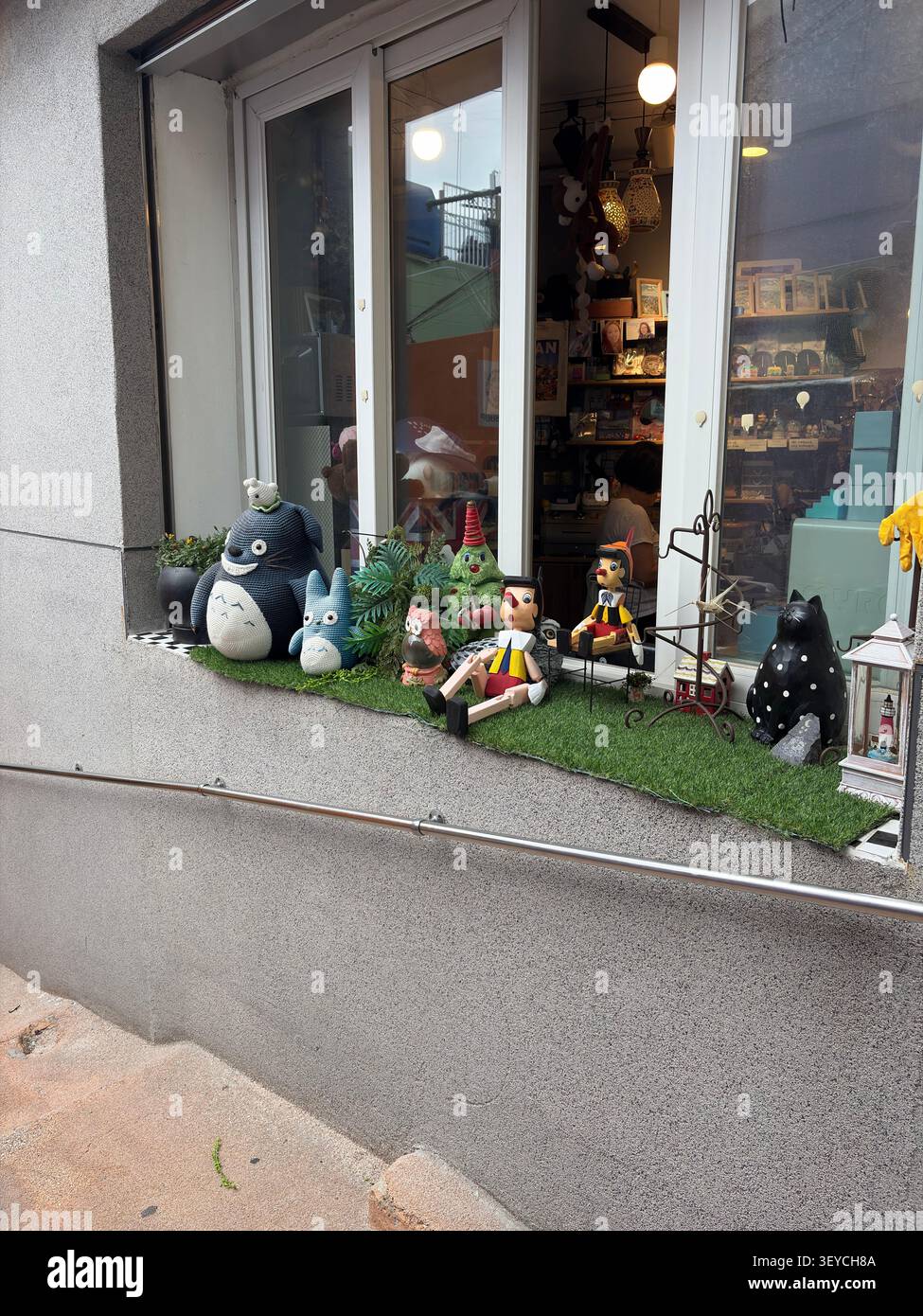 Bunte Figuren und dekorative Objekte, die vor einem antiken Schaufenster in Europa ausgestellt werden. - Smartphone-aufgenommenes Stockfoto