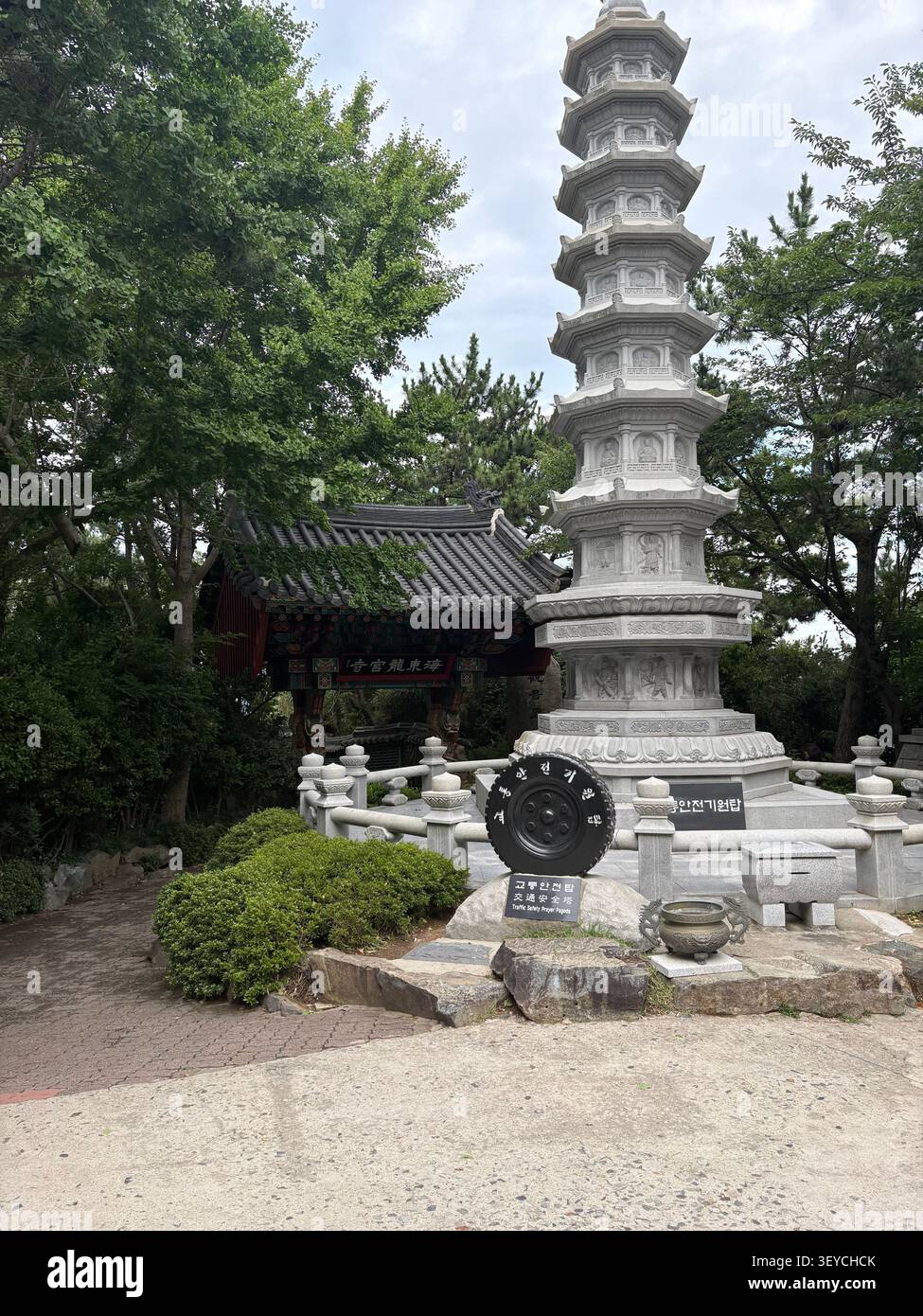 Mehrstufige Granitsteinpagode an einem buddhistischen Tempel in Südkorea, mit traditionellem Holztor und üppigen Bäumen im Hintergrund. Koreanische Zeichen VI - Smartphone-aufgenommenes Stockfoto