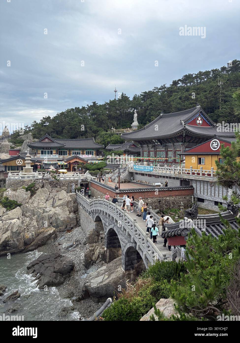 15. Juli 2025, Busan, Südkorea - Haedong Yonggungsa buddhistischer Tempelkomplex, erbaut auf felsigen Klippen am Meer mit Steinbrücke und Besuchern, South Kore - Smartphone-aufgenommenes Stockfoto