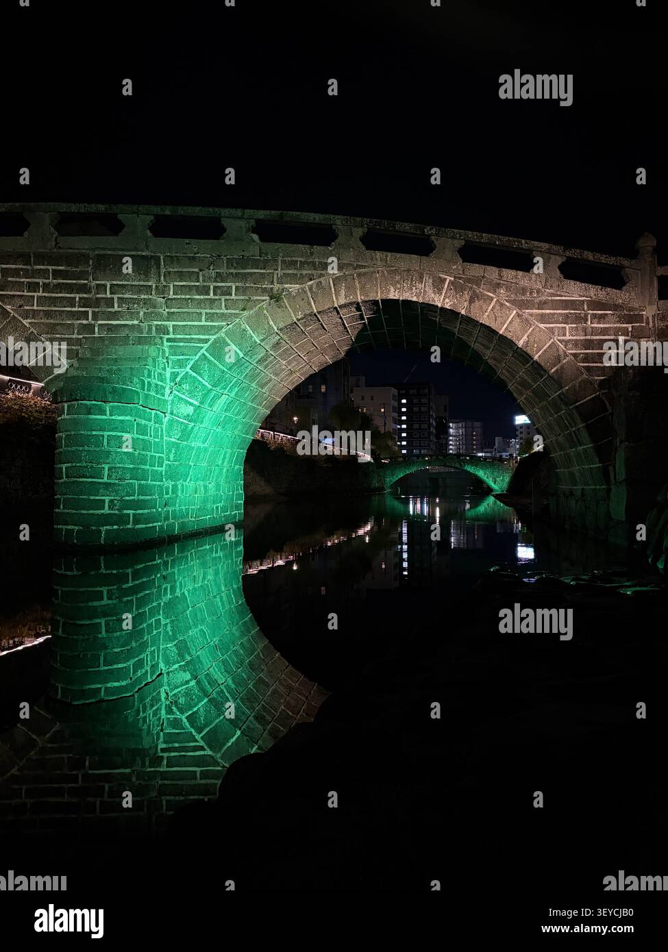 Historischer Stadttor-Bogen aus Stein, beleuchtet mit grünem Licht bei Nacht in China, dramatischer niedriger Winkel durch die kreisförmige Öffnung, die Stadtlichter b freigibt - Smartphone-aufgenommenes Stockfoto