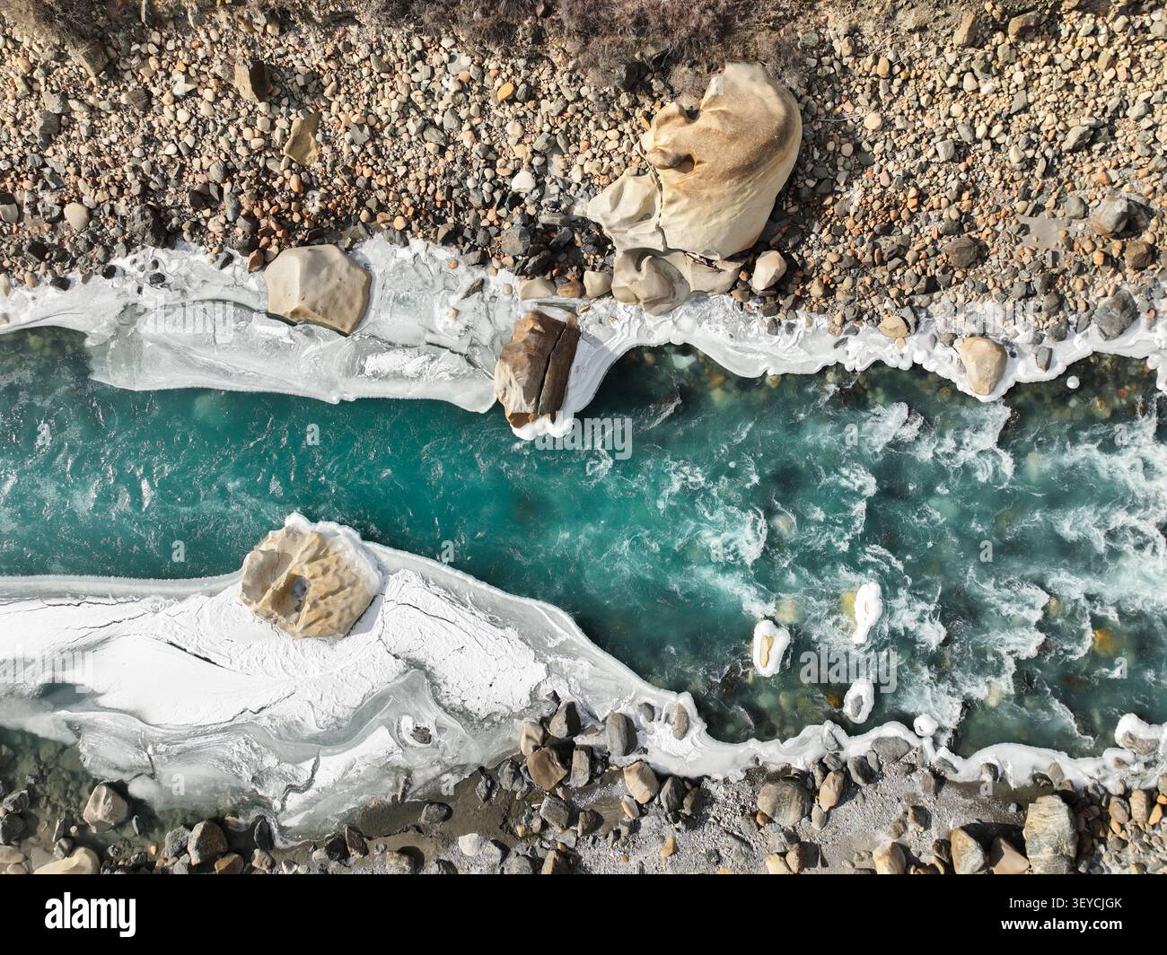 Blick von oben auf den pulsierenden türkisfarbenen Gletscherfluss, der zwischen dicken Schichten von weißem Eis und steilen, felsigen, bunten Ufern fließt Stockfoto