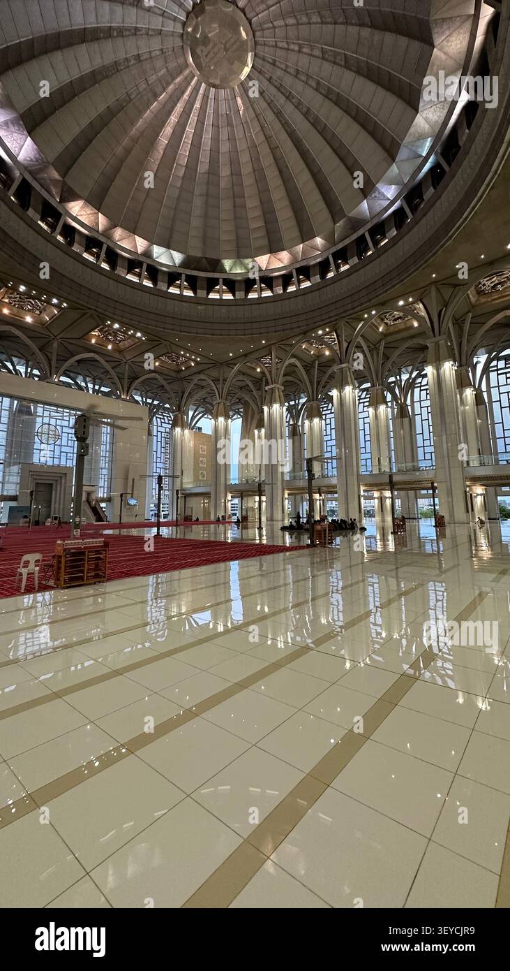 Das große Innere einer großen Moschee in Südostasien mit massiver Betonkuppel, Marmorböden mit Reflexionen, gotischen Bögen und rotem Gebetsteppich - Smartphone-aufgenommenes Stockfoto