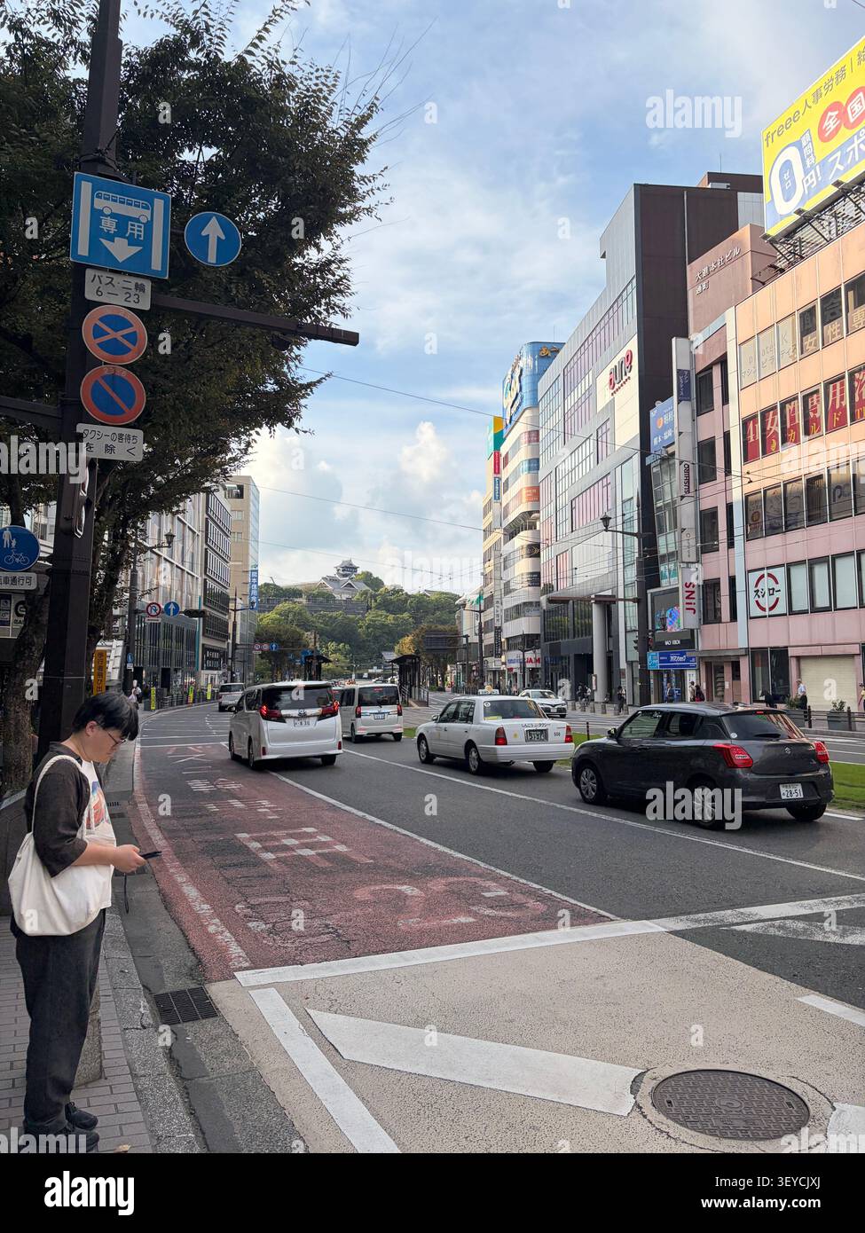 16. Oktober 2025, Japan - geschäftige japanische Stadtstraße mit Geschäftsgebäuden, japanischen Straßenschildern, Busspurmarkierungen und Fußgängern mit Smartphone. - Smartphone-aufgenommenes Stockfoto