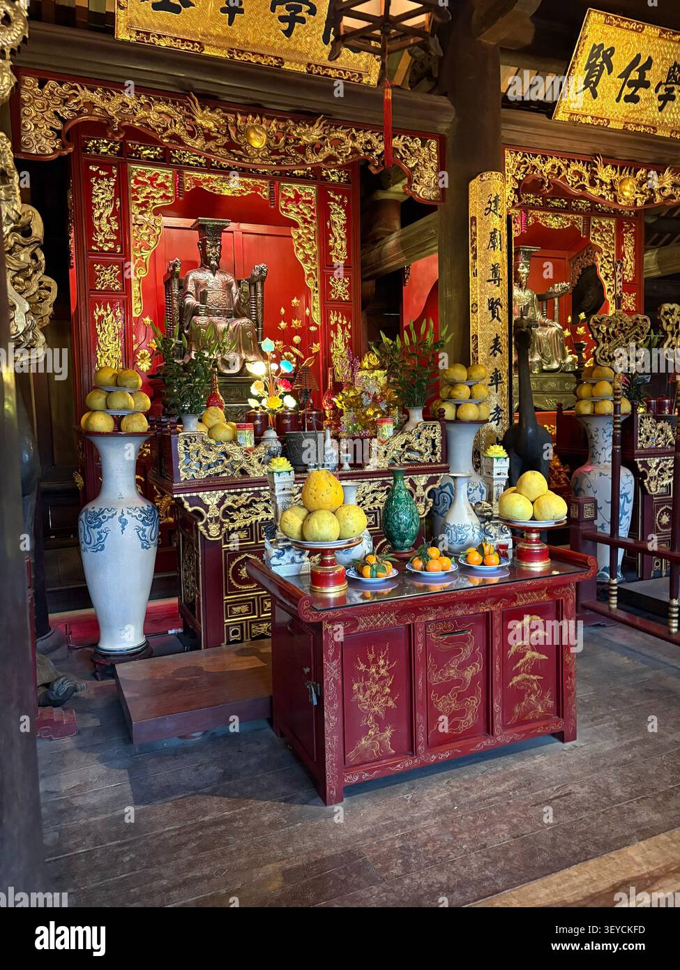 Blick von oben auf den verzierten vietnamesischen Tempelaltar mit rotem Lack, Goldschnitzereien, Bronzestatuen, Keramikvasen und frischen Obstopfern. Vietna - Smartphone-aufgenommenes Stockfoto