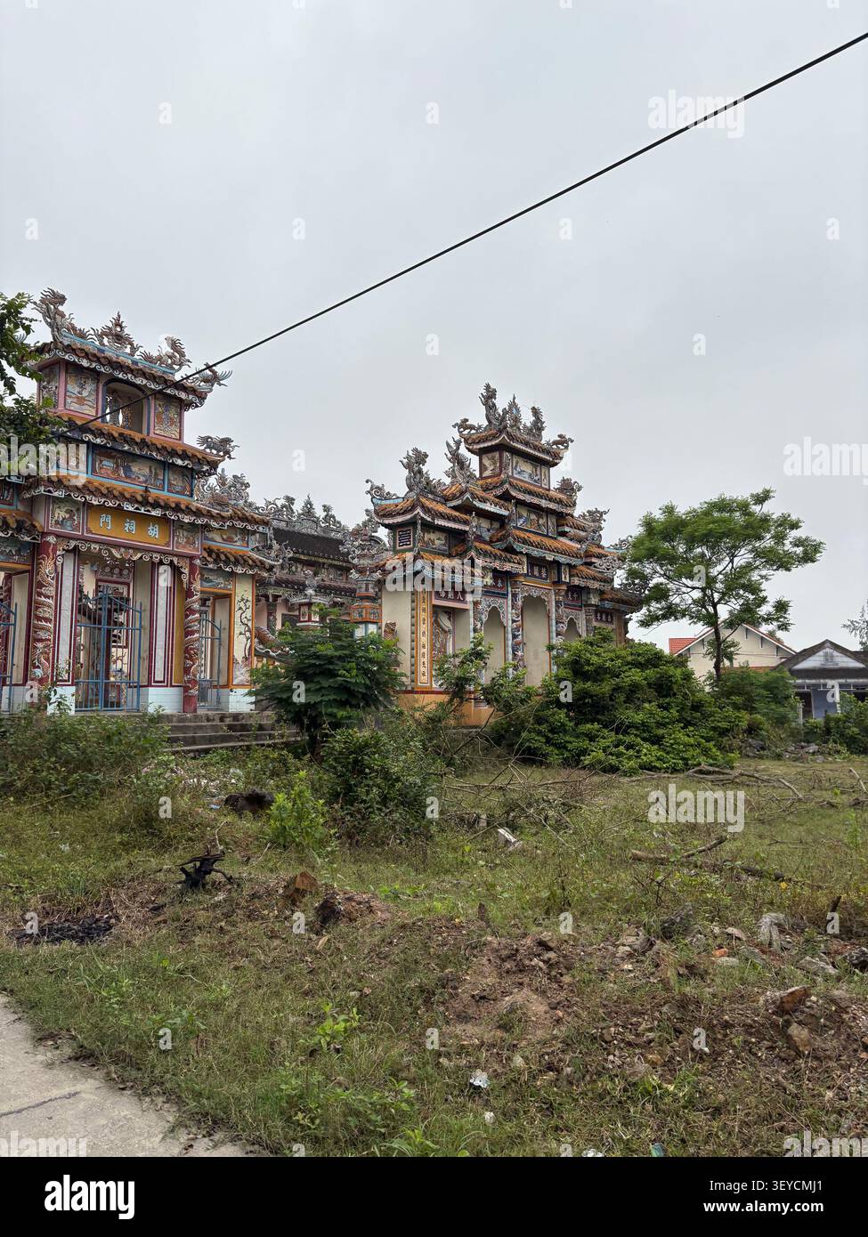 Reich verzierte chinesisch-vietnamesische Tempelfassade mit Drachendach-Ornamenten, farbenfrohen Wandmalereien und chinesischen Schriftzeichen, Vietnam. Bedeckter Himmel, Dokumentarfilm - Smartphone-aufgenommenes Stockfoto