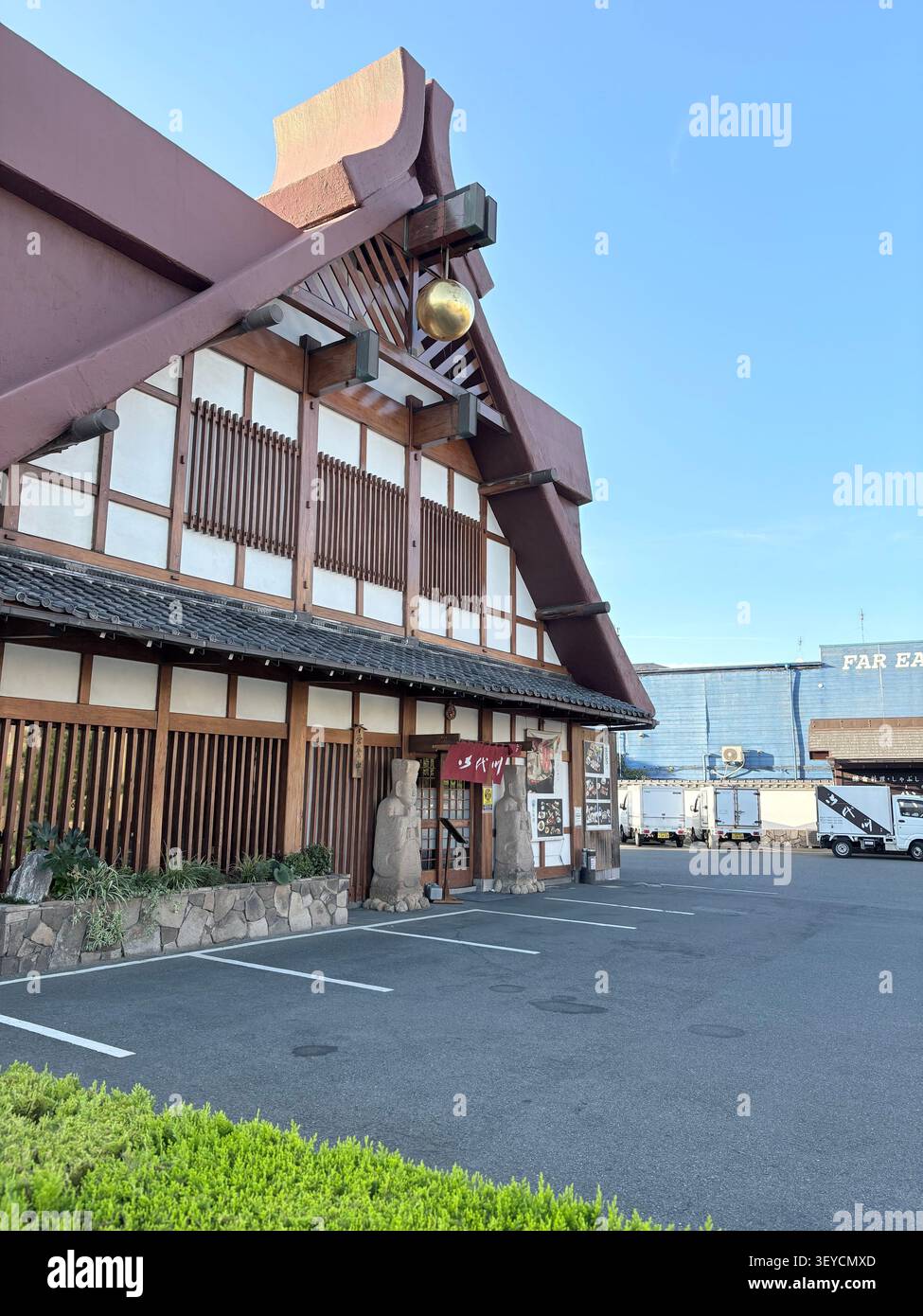 Traditionelles japanisches Restaurant mit dunkler Holzgitterfassade, Shoji-Paneelen, geschwungenen Dachdetails und roten Bannern mit Kanji-Text. Japan. - Smartphone-aufgenommenes Stockfoto